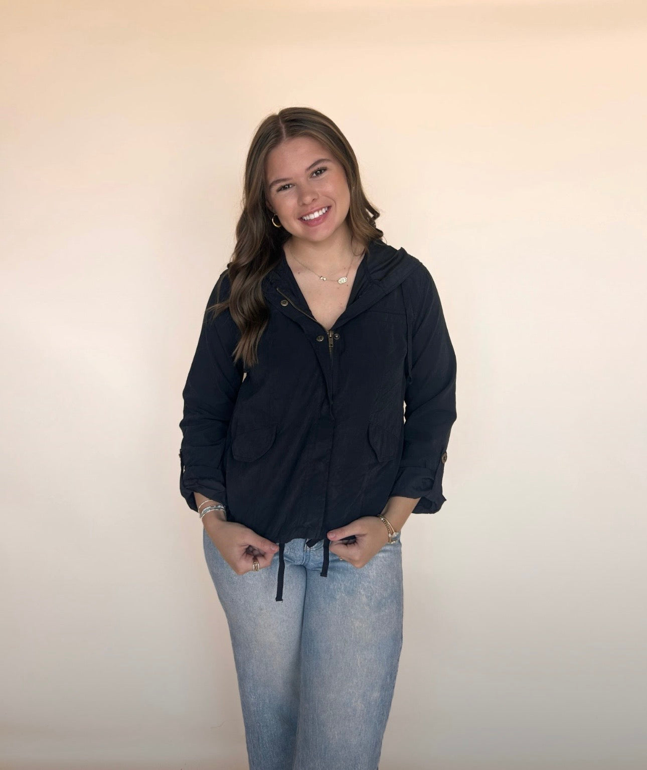 Woman wearing a black hoodie and light blue jeans against a plain background
