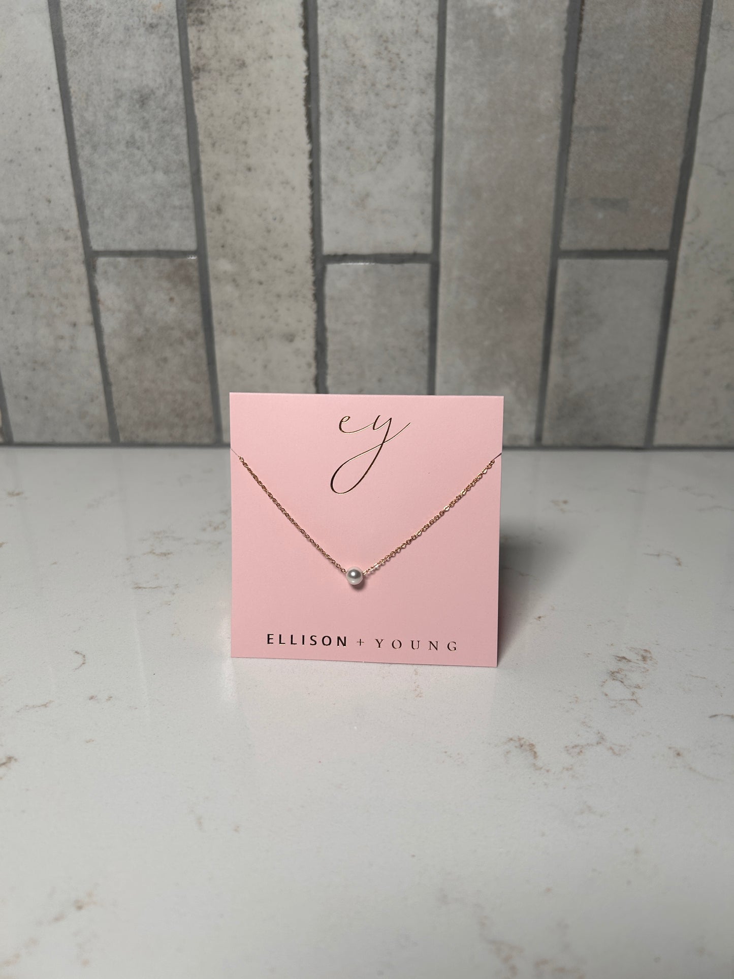 Dainty single pearl necklace on a gold chain by Ellison + Young, minimalist everyday jewelry displayed on pink card