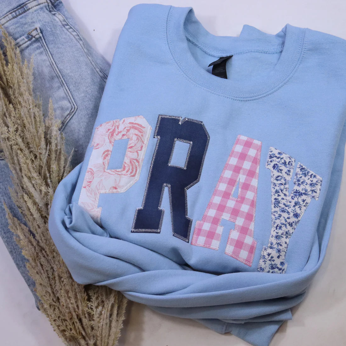 Light blue sweatshirt with decorative letters on a white background