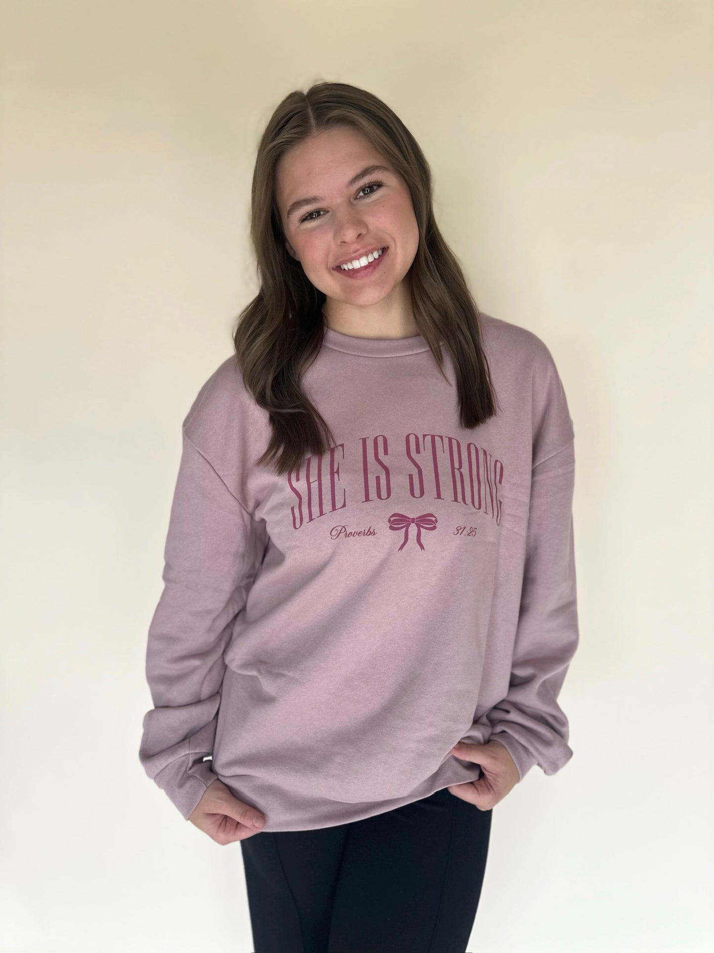 Person wearing a pink sweatshirt with 'She is Strong' text on a plain background