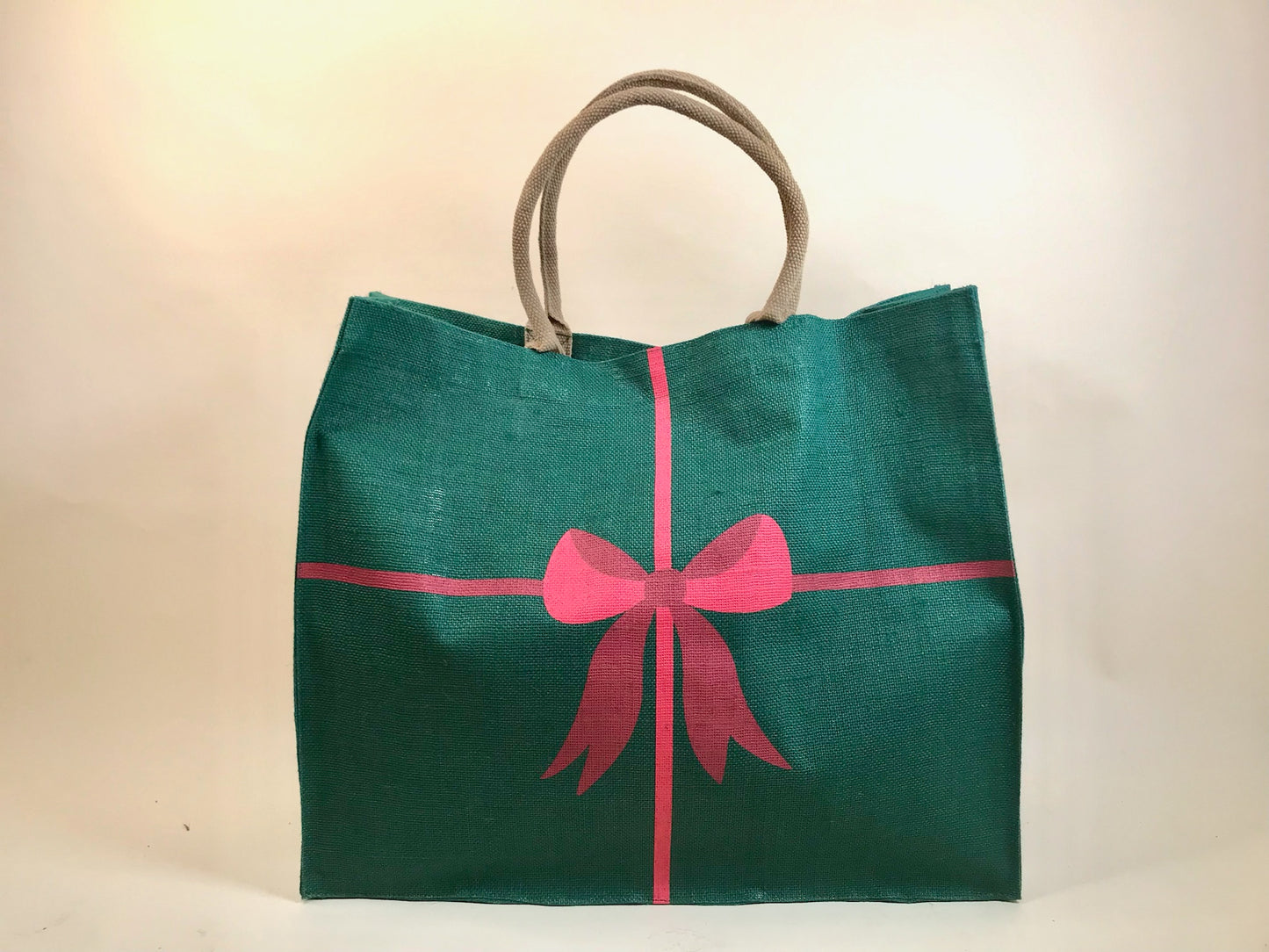 Large green holiday tote bag with red bow and ribbon design, rope handles shown against neutral background
