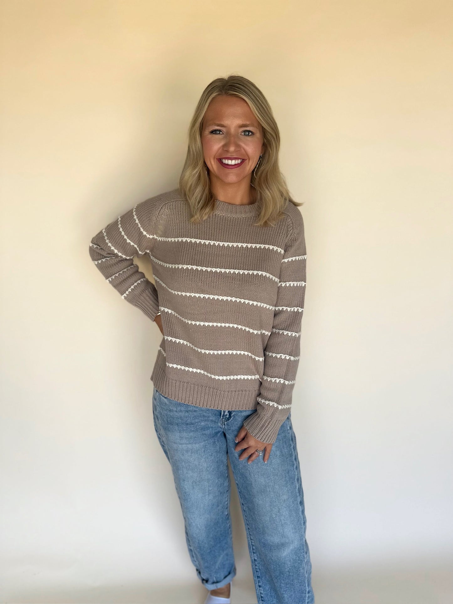 Woman wearing a striped sweater and jeans against a plain background