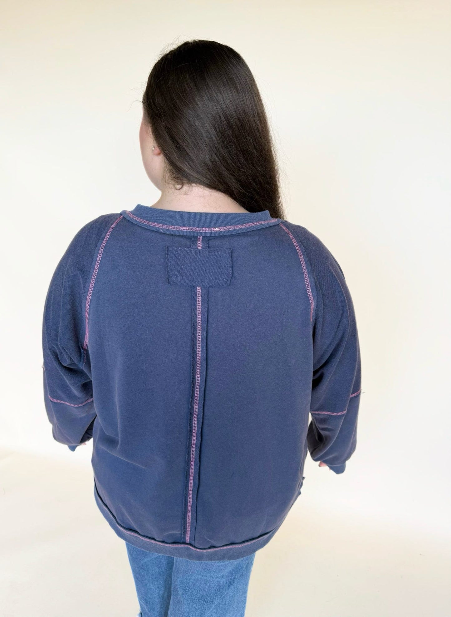 Back view of a navy long-sleeve top featuring pink contrast stitching, a center back seam, and a relaxed fit.