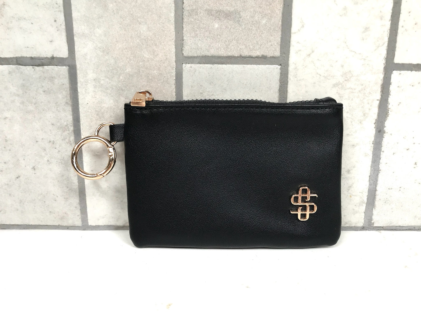 Black pouch with gold zipper and key ring on a tiled background