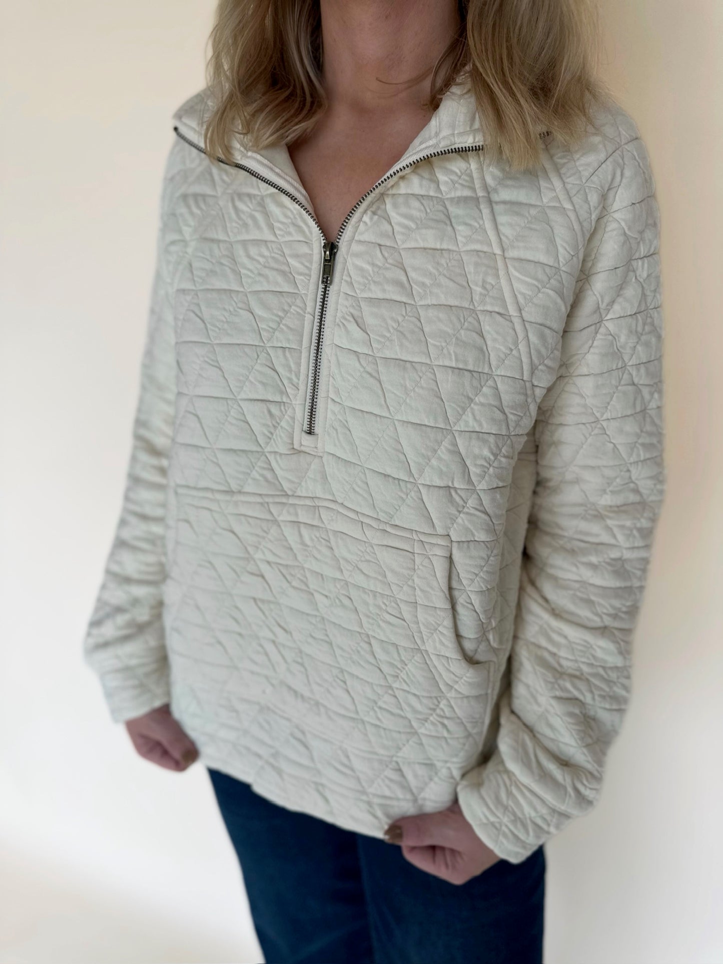 Person wearing a textured cream pullover with a zipper on a plain background