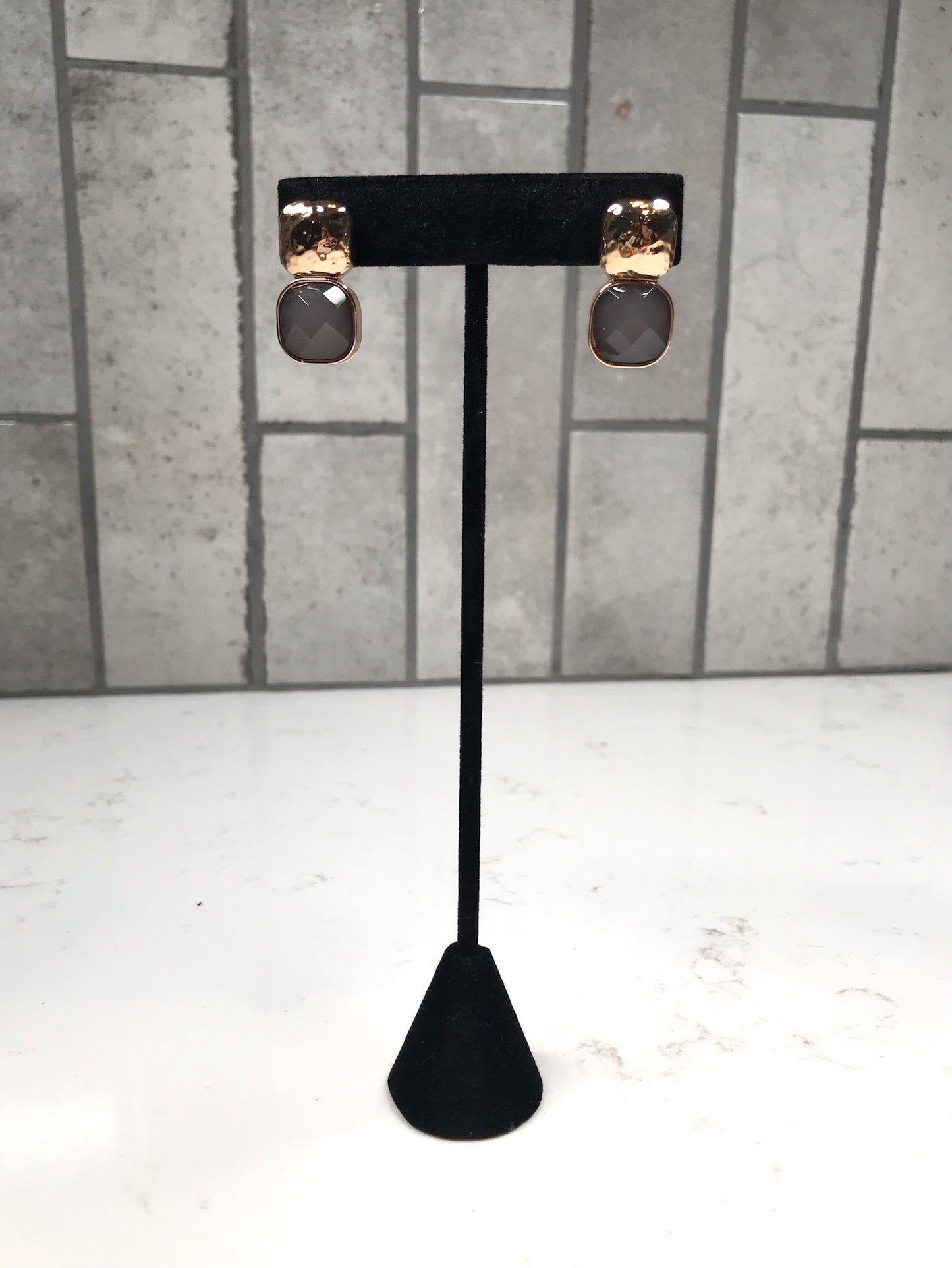 Gold hammered stud earrings with faceted gray drop stones displayed on a black stand.