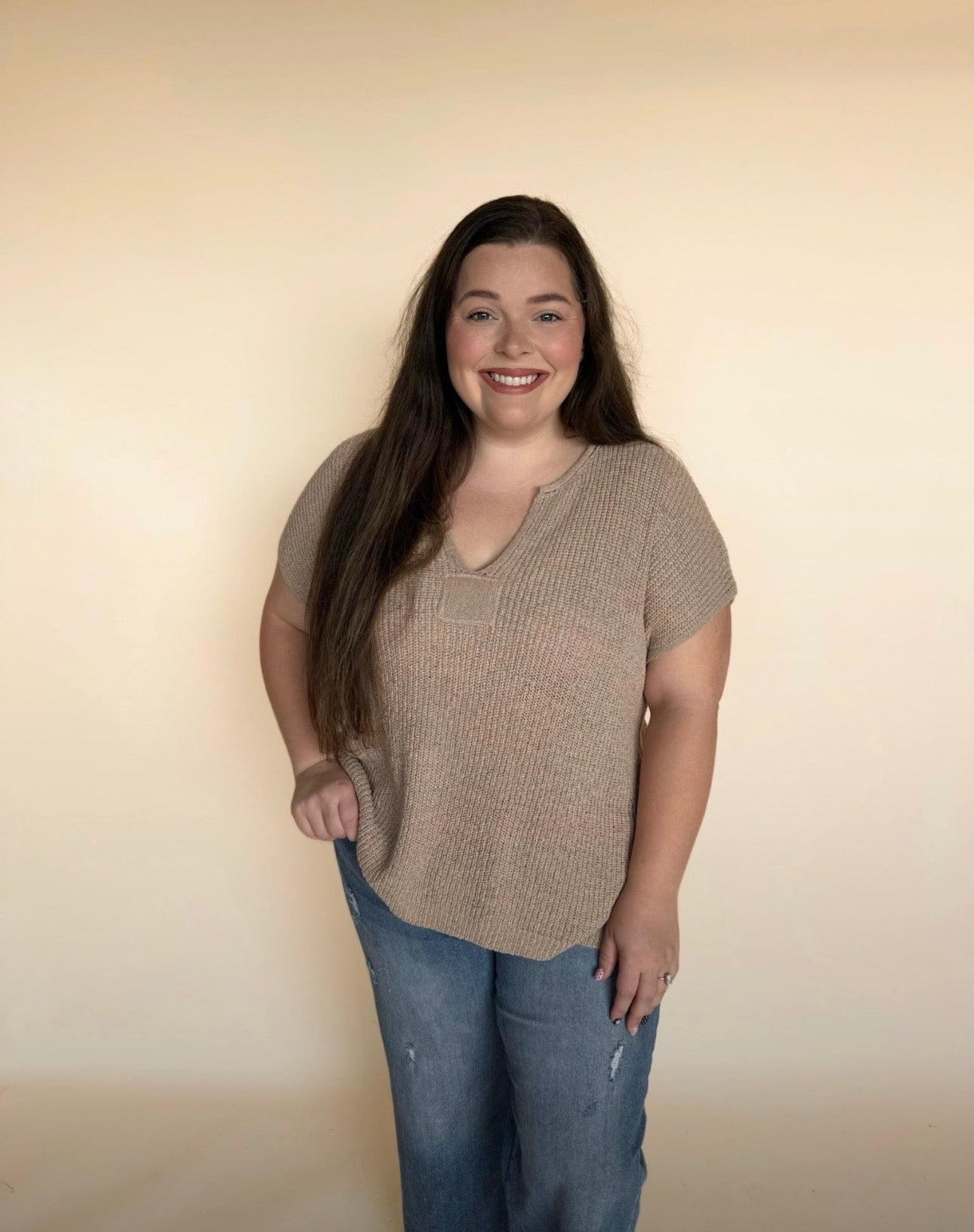 Woman wearing a light tan short-sleeve top and blue jeans against a beige background