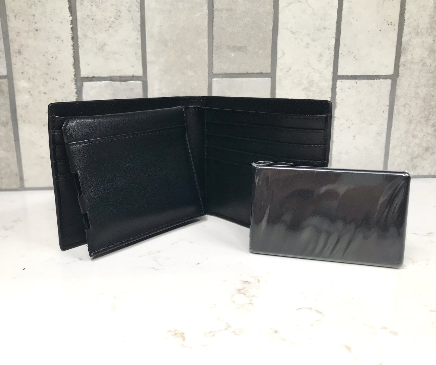 Black leather wallet and cardholder on a light surface with a tiled wall background