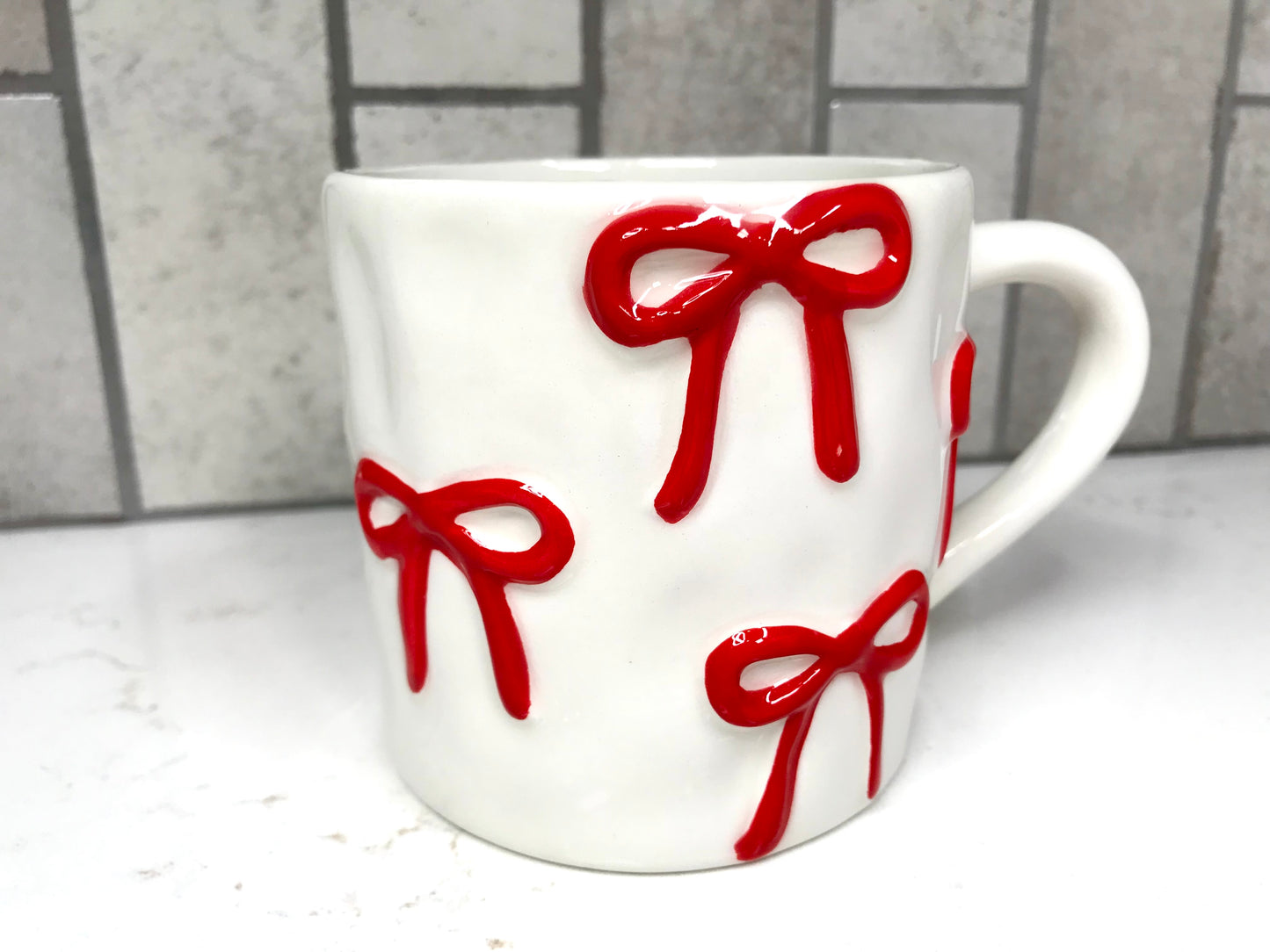 White mug with red bows on a white surface and tiled wall background