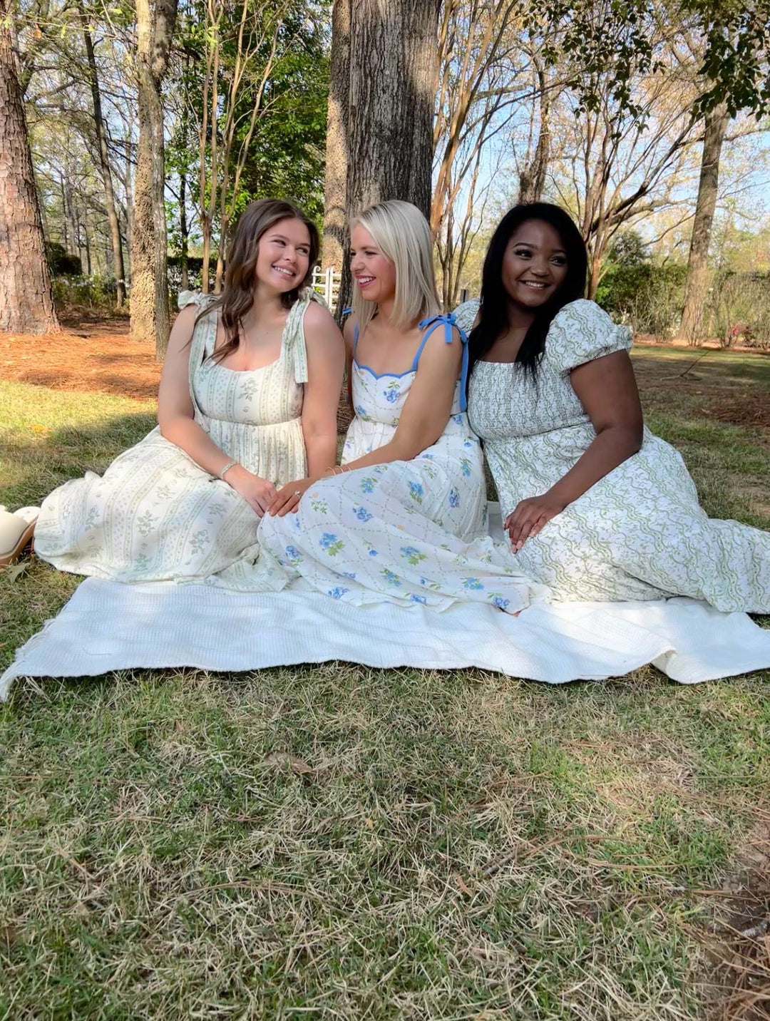 Women’s garden party dresses in soft floral prints and pastel tones, styled outdoors on blanket, spring boutique collection