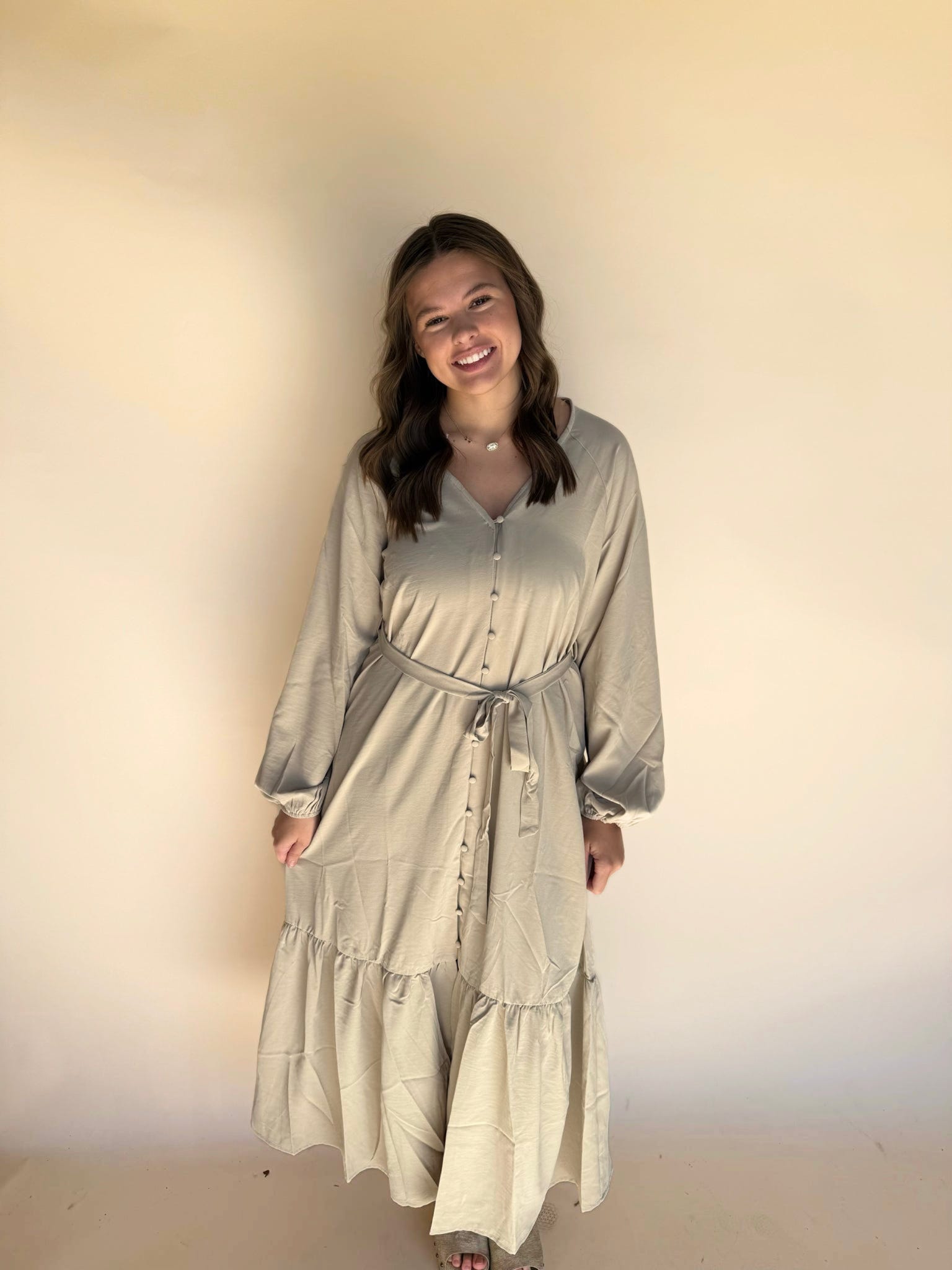 Woman wearing a long, light-colored dress against a plain background