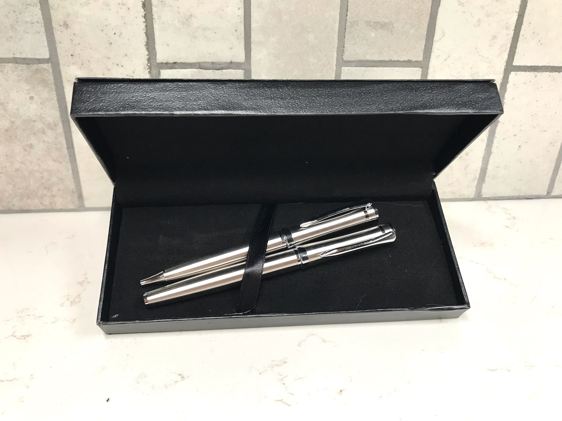 Two silver pens in a black box on a tiled floor
