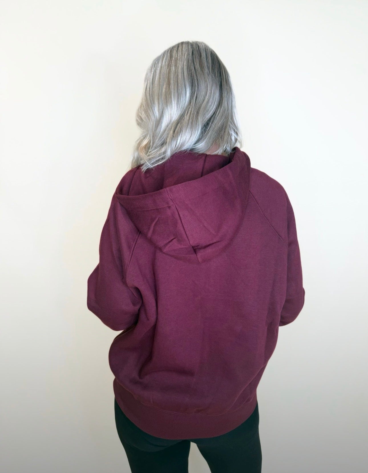 Woman wearing maroon zip-up hoodie with pockets, casual fit paired with black leggings against neutral backdrop.