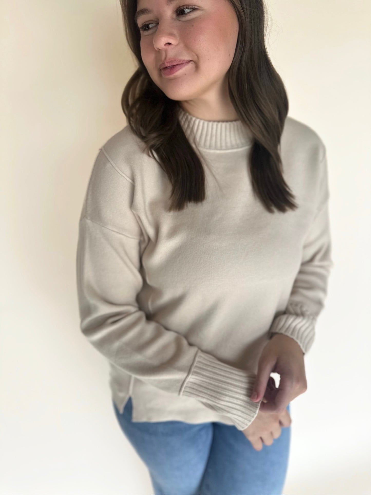 Woman wearing a oatmeal sweater and blue jeans against a plain background