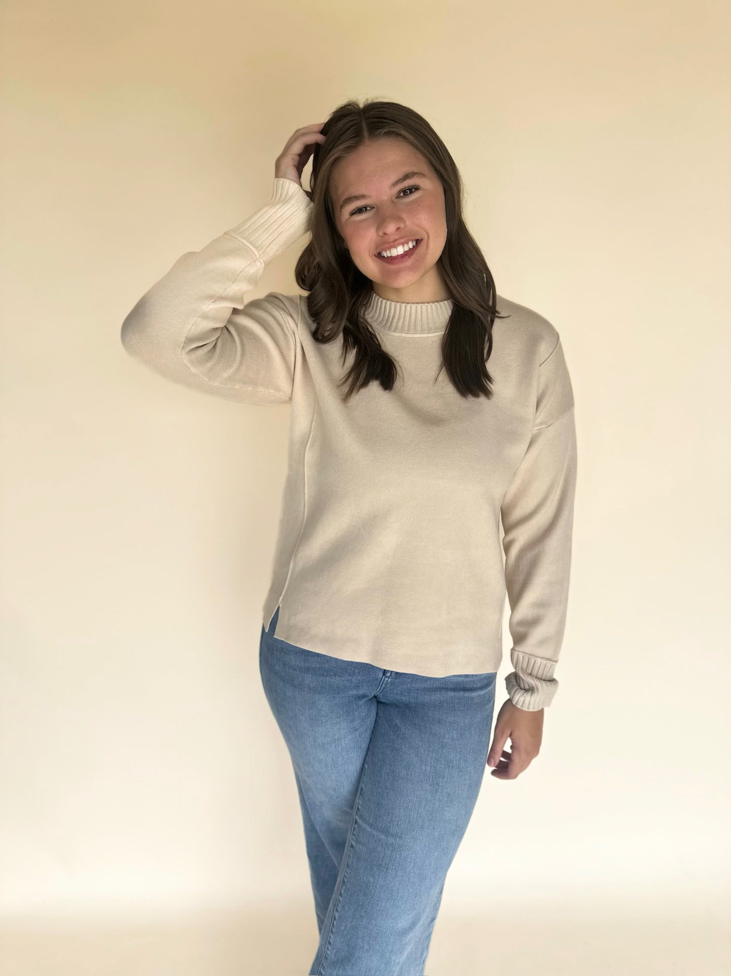 Woman wearing an oatmeal sweater and blue jeans against a plain background