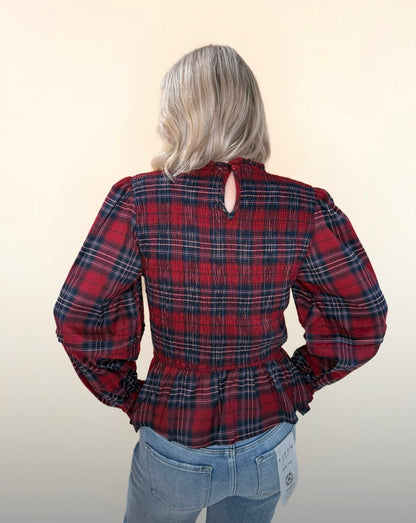 Back view of red and navy plaid smocked blouse with puff sleeves, peplum waist, and keyhole button closure, paired with light wash jeans.