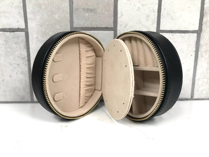 Round black jewelry box with beige interior on a tiled floor background