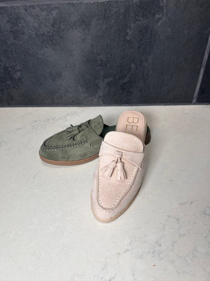Pair of suede loafers, one green and one pink, on a light surface with a dark background.
