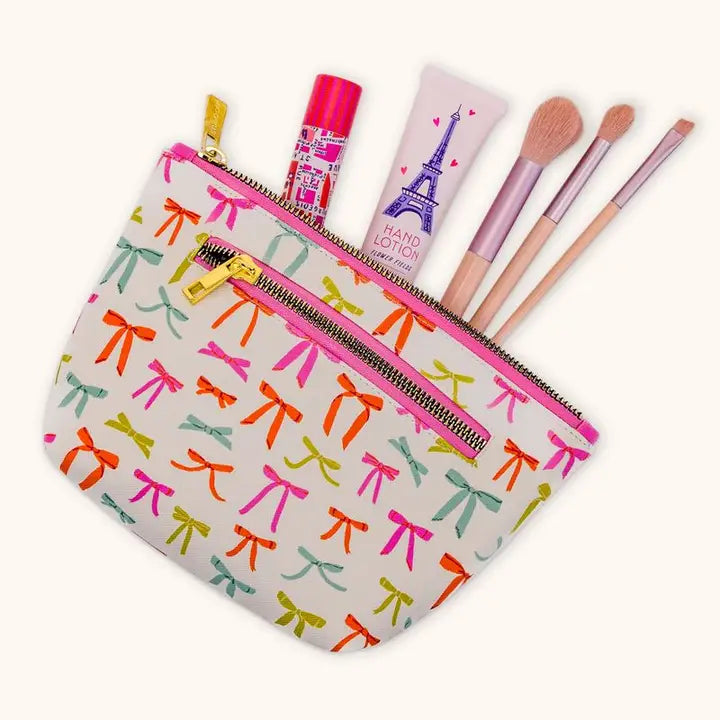 Bow print cosmetic makeup bag filled with brushes and beauty products, cute boutique travel makeup pouch gift