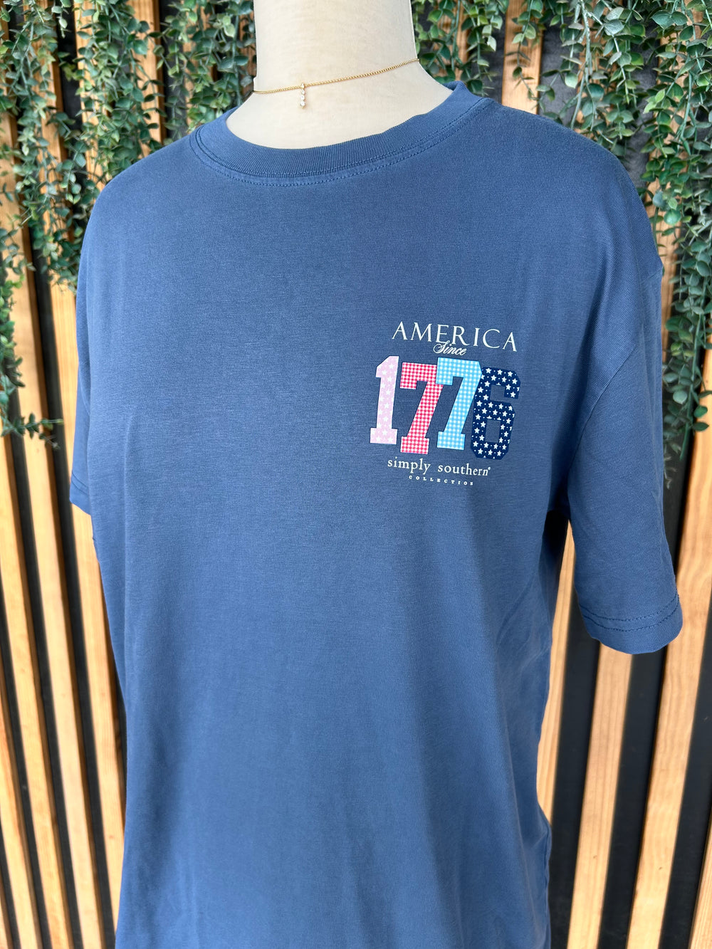 Front of a Simply Southern navy blue crew neck Youth T-shirt with a small "America Since 1776" patriotic graphic on the left chest featuring floral, gingham, and star-print numbers.