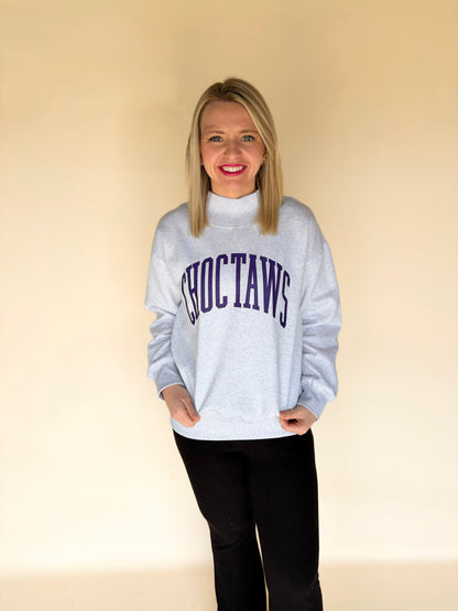 Full body view of woman modeling light gray Choctaws mock neck sweatshirt with purple varsity lettering, oversized boutique pullover sweatshirt