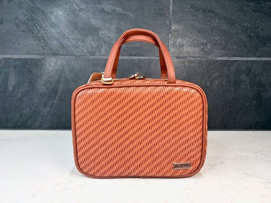 Stephanie Johnson cognac textured cosmetic travel bag with top handles and zip closure displayed on a countertop with dark tile background.