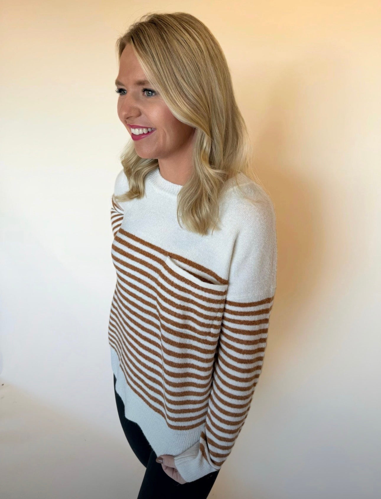 Woman wearing a white and brown striped sweater against a plain background