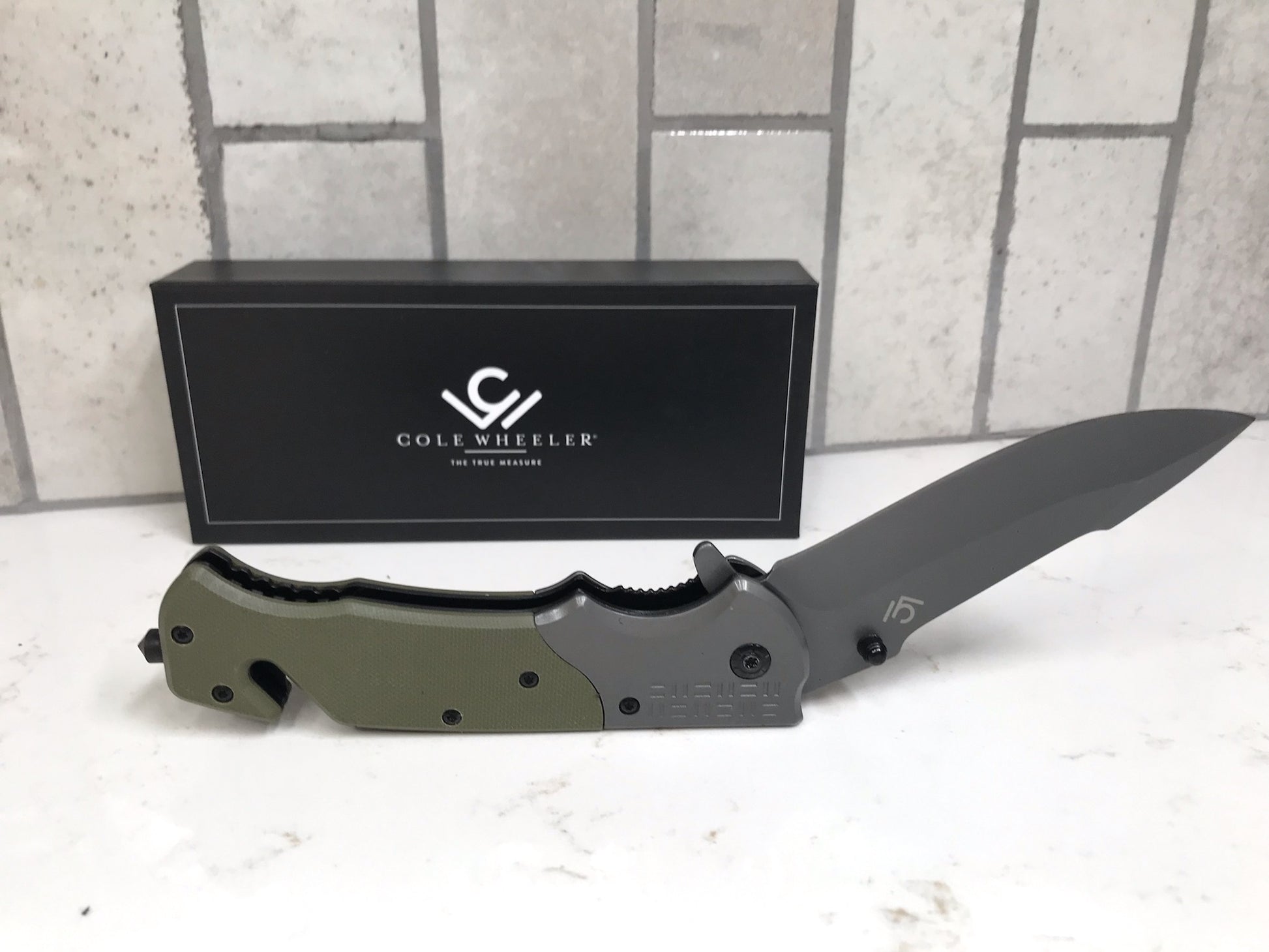 Folding knife with a black sheath on a white surface, Cole Wheeler brand visible