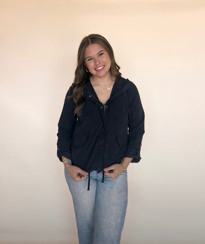 Woman wearing a black hoodie and light blue jeans against a plain background