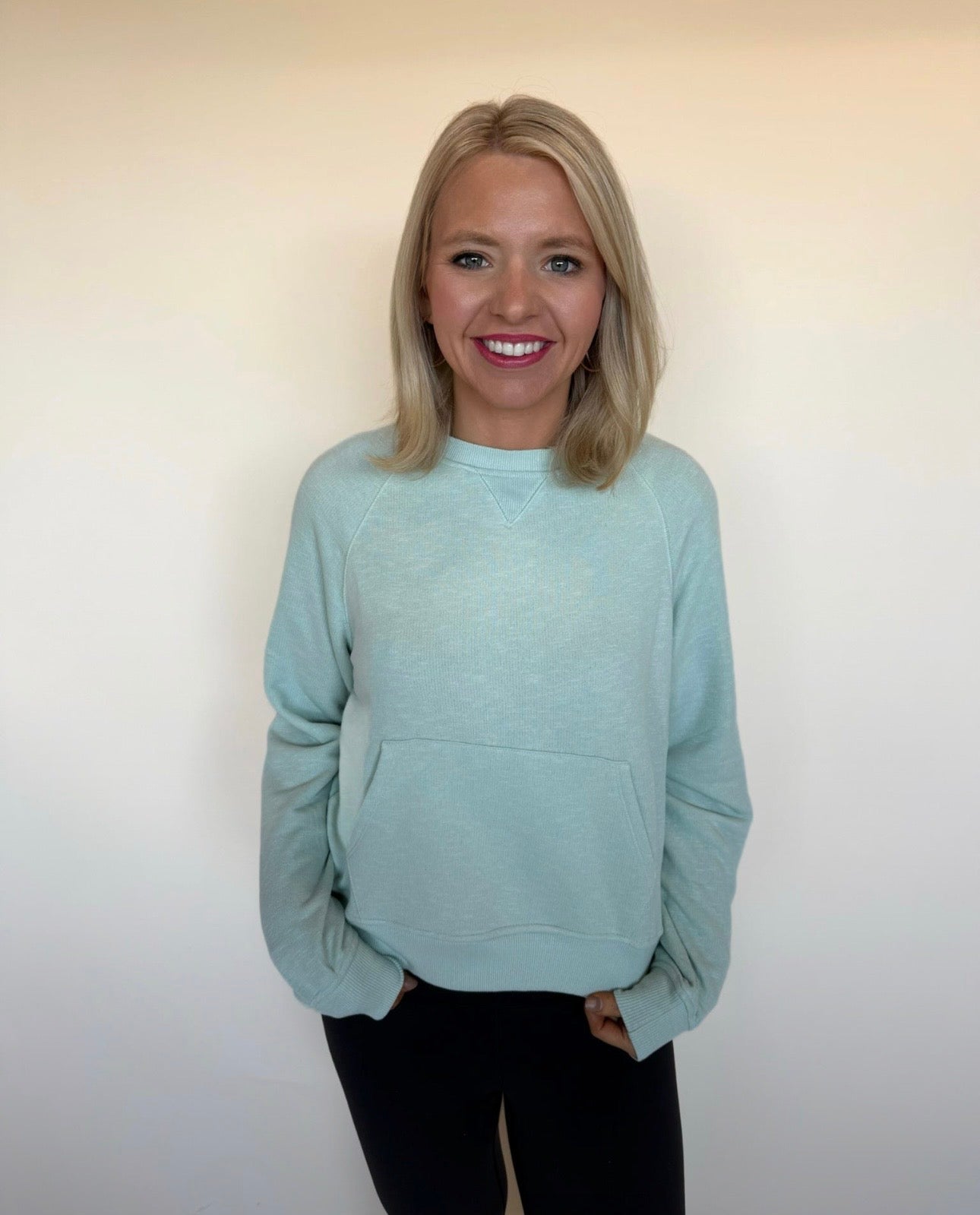 Woman wearing a mint sweatshirt against a plain background