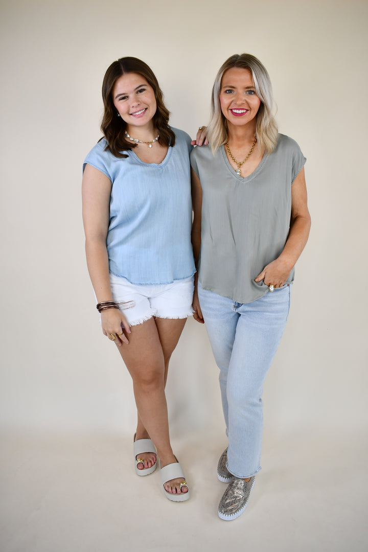 Two women wearing the Dear John Yanis V-Neck Cap Sleeve Top in Skyway Light Wash and Iceberg Green, styled with denim shorts and jeans.