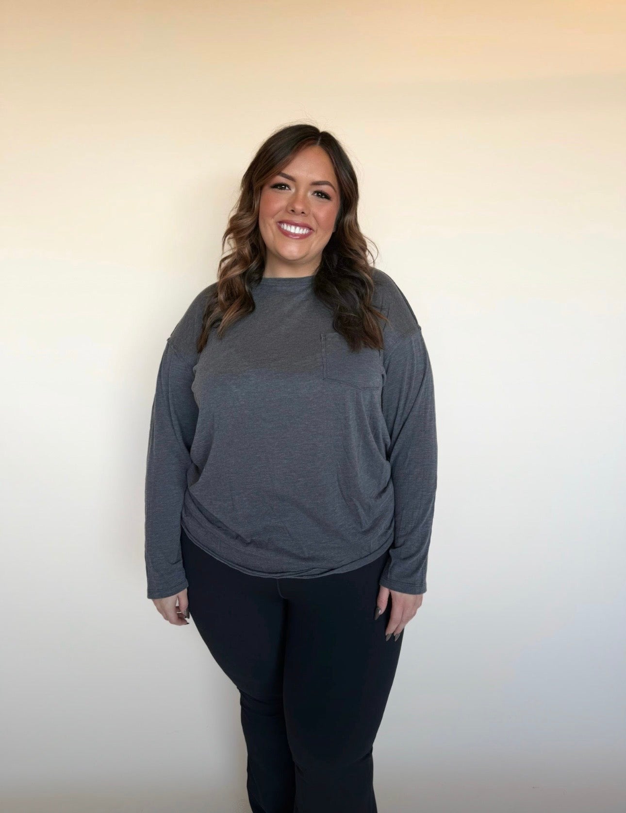 Woman wearing a gray long-sleeve top and black pants against a plain background