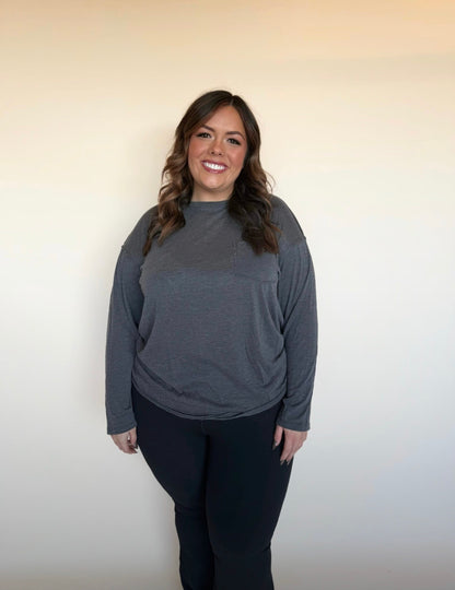 Woman wearing a gray long-sleeve top and black pants against a plain background