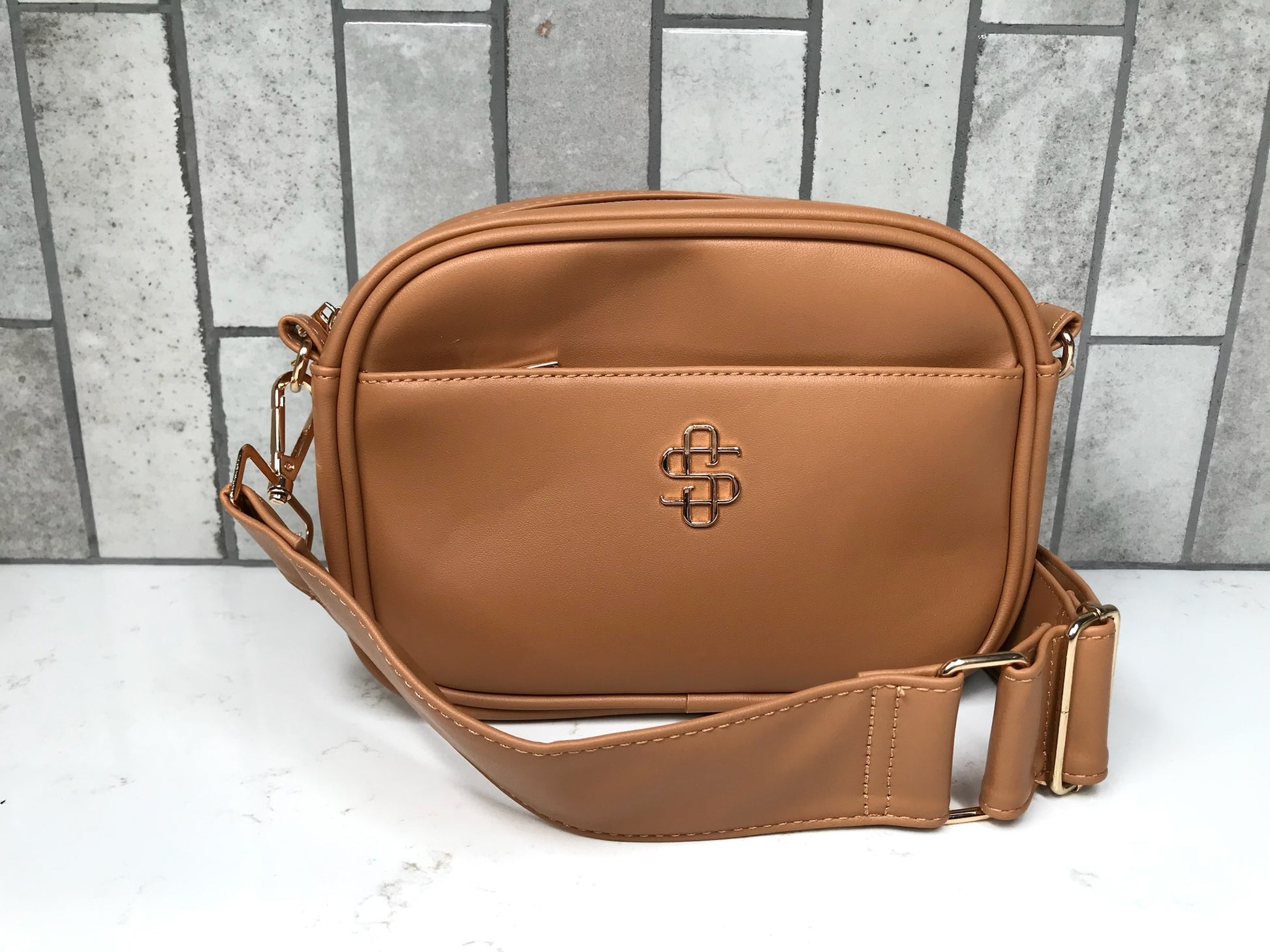 Brown leather crossbody bag with a visible brand logo on a light gray background