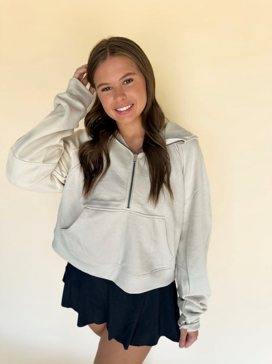 Woman wearing a light gray zip-up hoodie and dark shorts against a beige background