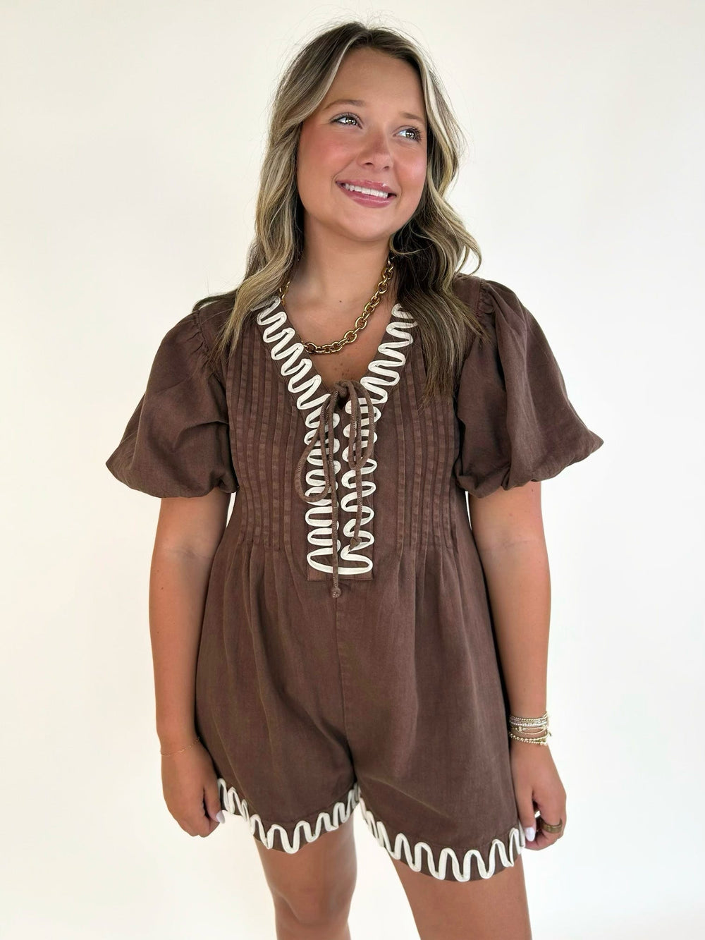 Women's brown puff sleeve romper featuring white embroidered trim, V-neckline, and relaxed fit.