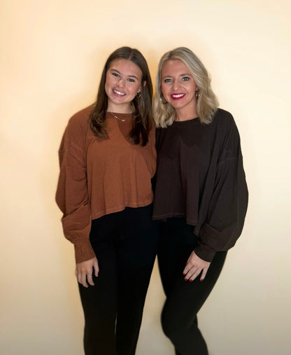 Two women wearing oversized long sleeve tops, one in warm brown and one in dark chocolate brown, both paired with black pants for a casual fall outfit.