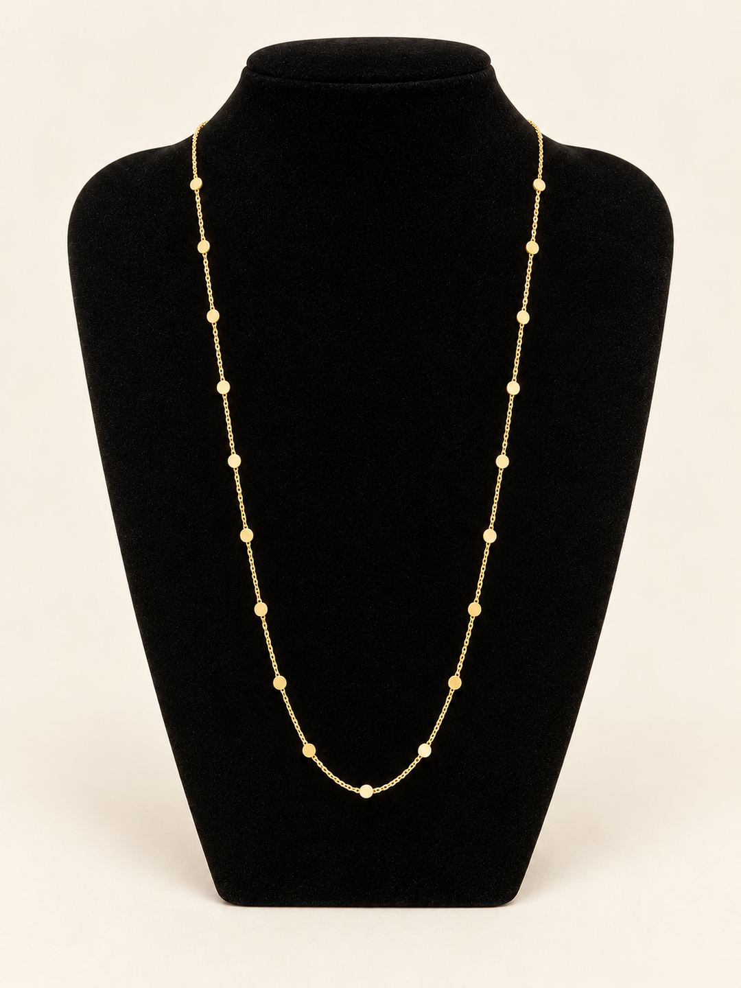 Long gold flat disc station chain necklace displayed on a black velvet jewelry bust with delicate evenly spaced round accents.