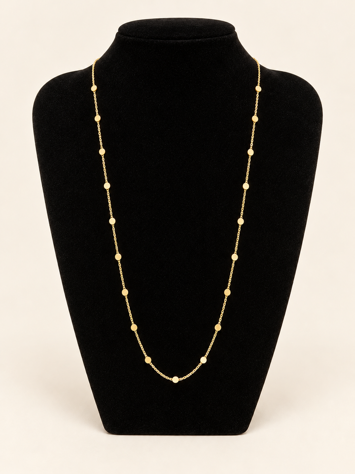 Long gold flat disc station chain necklace displayed on a black velvet jewelry bust with delicate evenly spaced round accents.