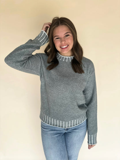 Woman wearing a light blue sweater with white trim against a beige background