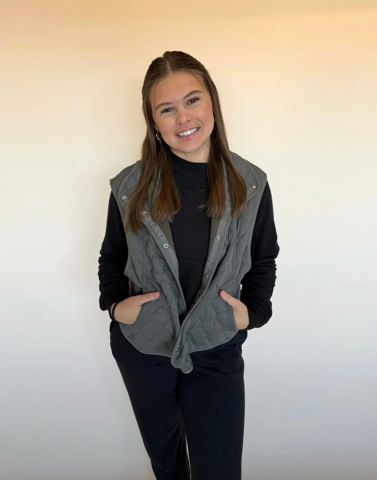 Person wearing a gray vest over a black outfit against a plain background