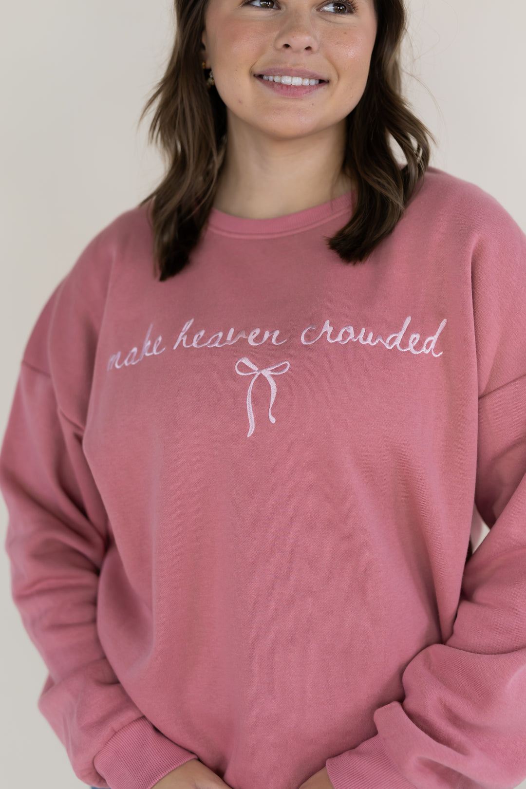 A woman wearing a dusty rose pink crewneck sweatshirt with the phrase &