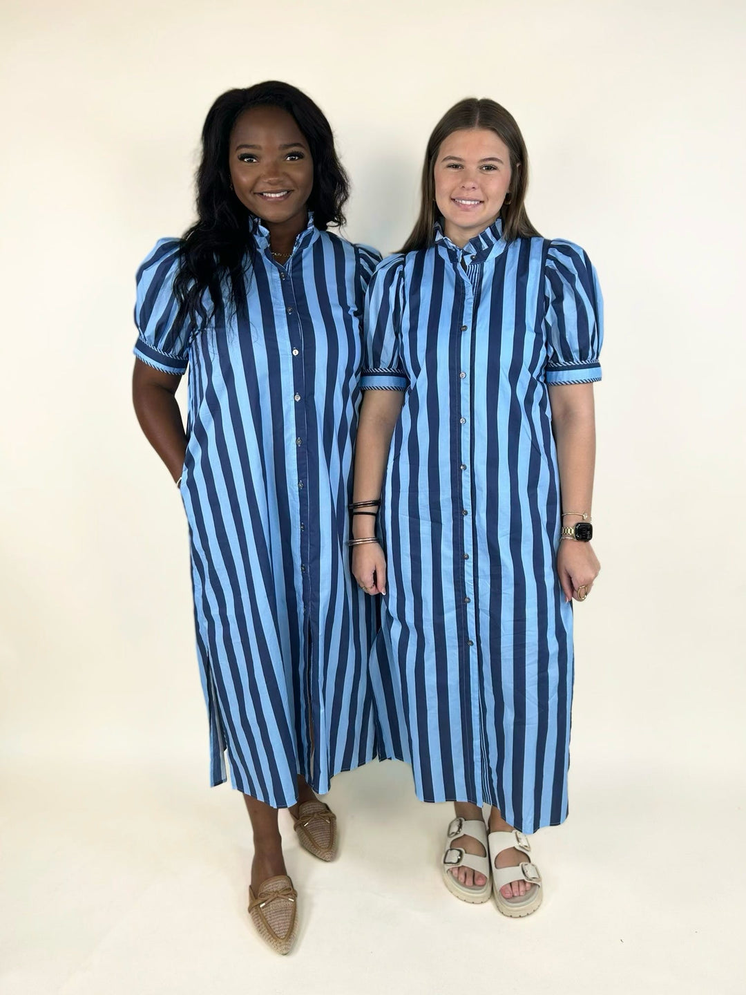 Two models wearing a blue striped button-front midi shirt dress with a ruffle mock neckline, puff sleeves, side pockets, and side slits, showcasing the relaxed fit on different body types.
