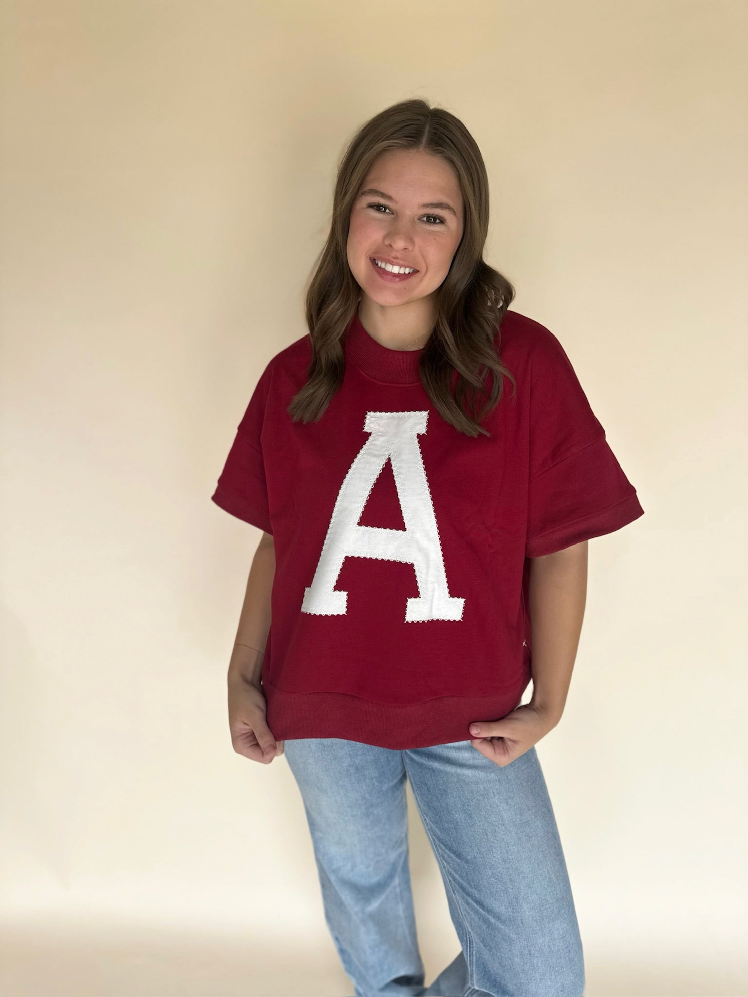 Person wearing a red sweatshirt with a white letter 'A' on a beige background