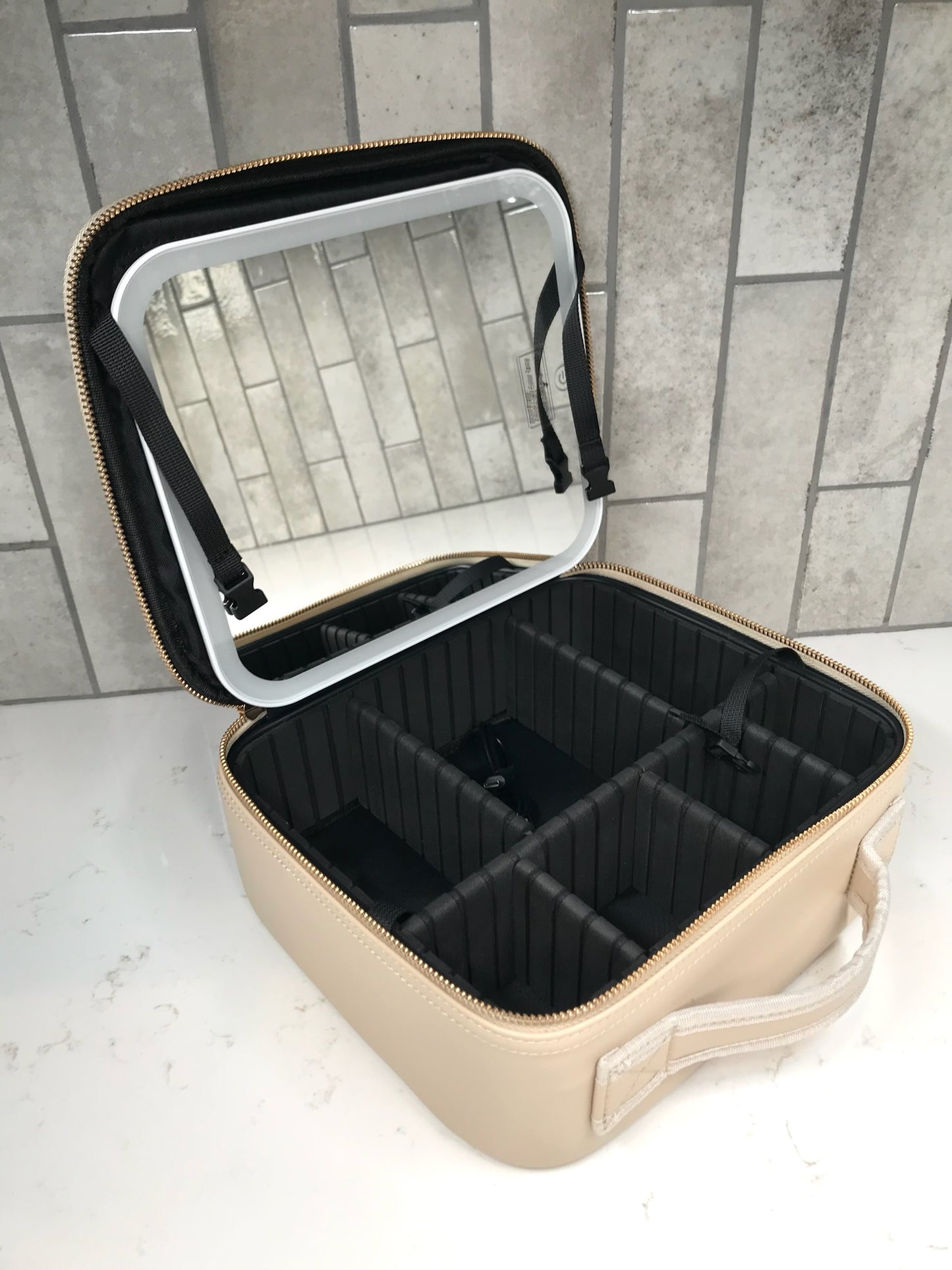 Beige travel cosmetic case with black interior compartments on a tiled floor.