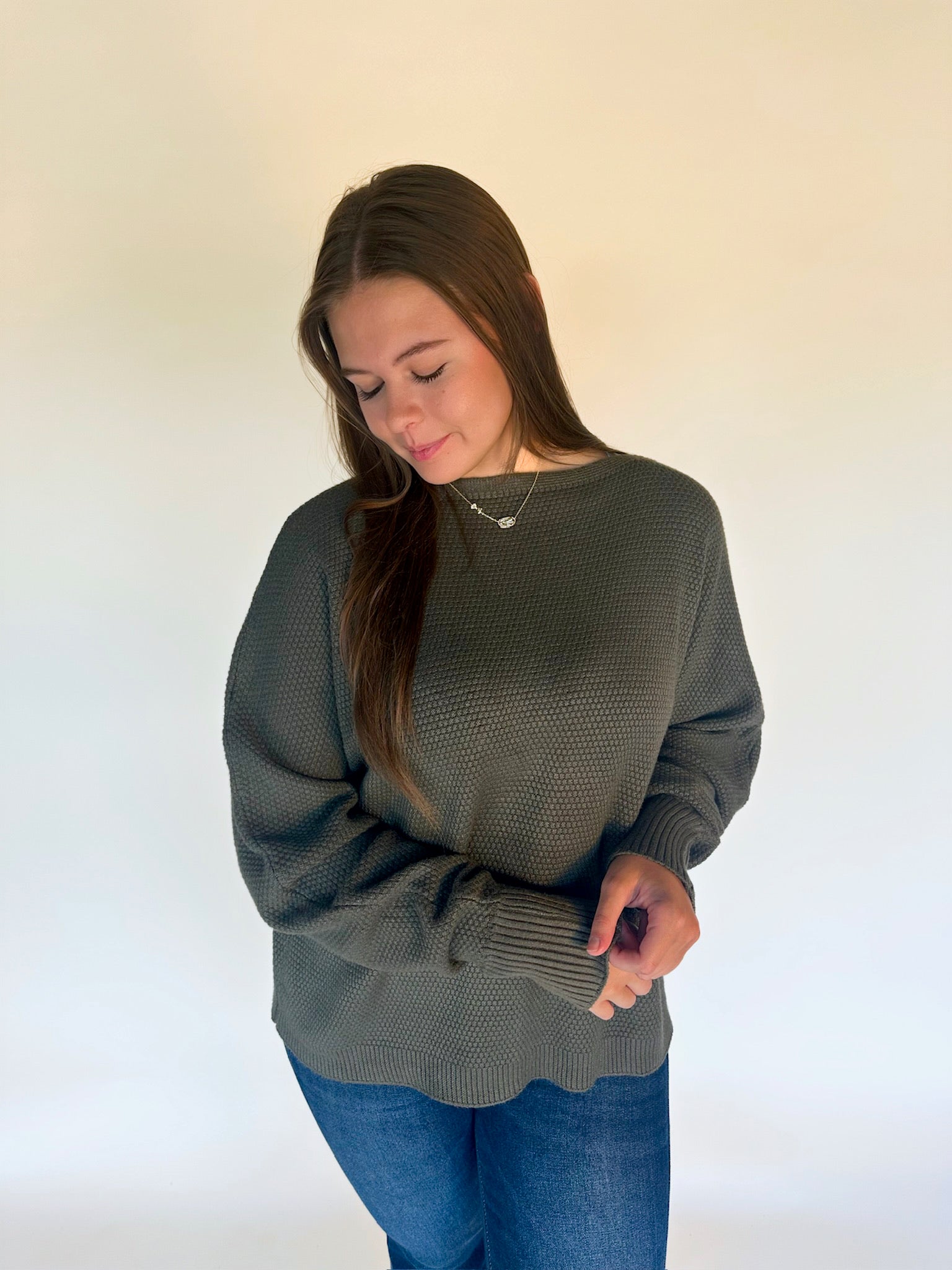 Woman wearing a green sweater and blue jeans against a white background
