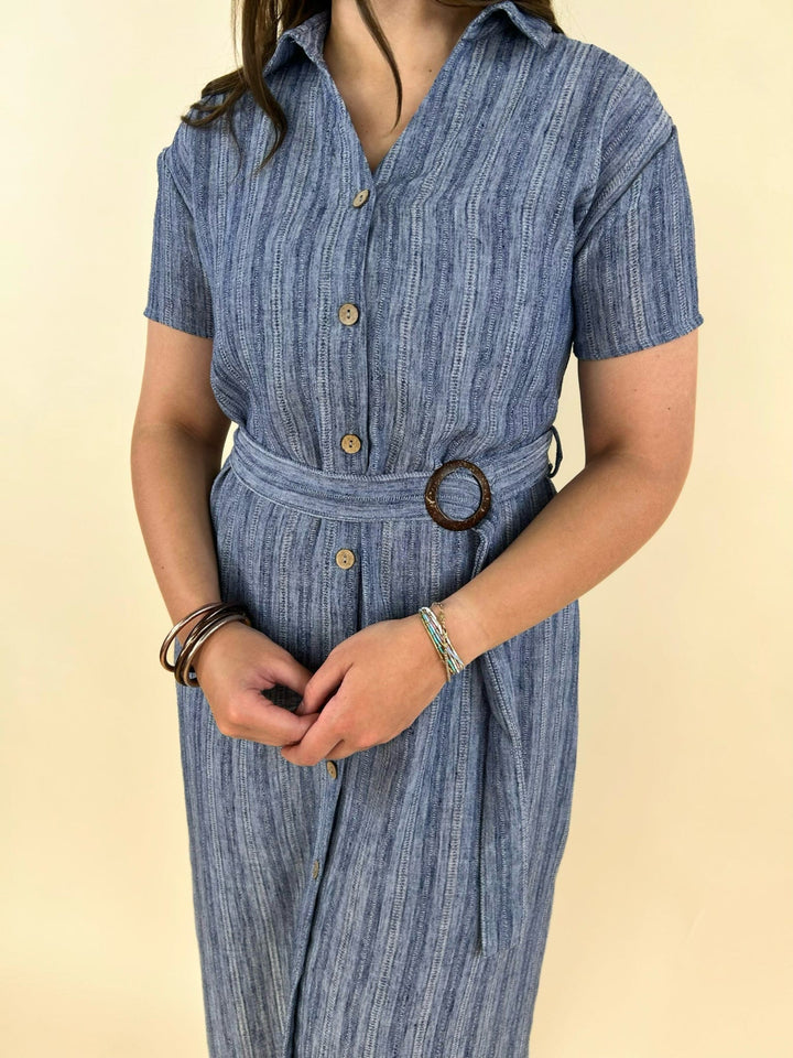 Close-up of blue striped shirt dress fabric with button front and round belt buckle detail, textured lightweight material