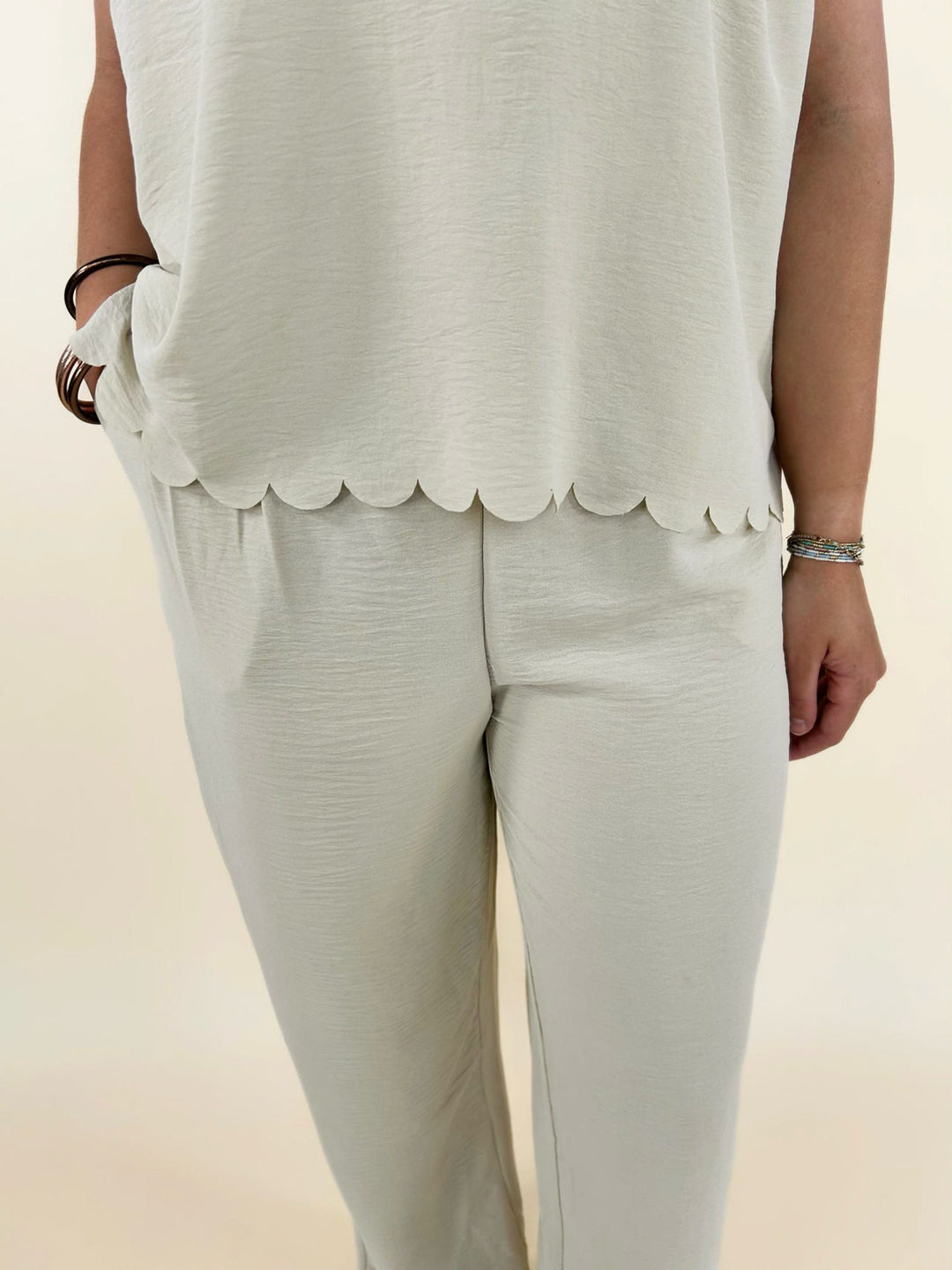 Close up front view of cream wide leg pants with scalloped hem top and pocket detail