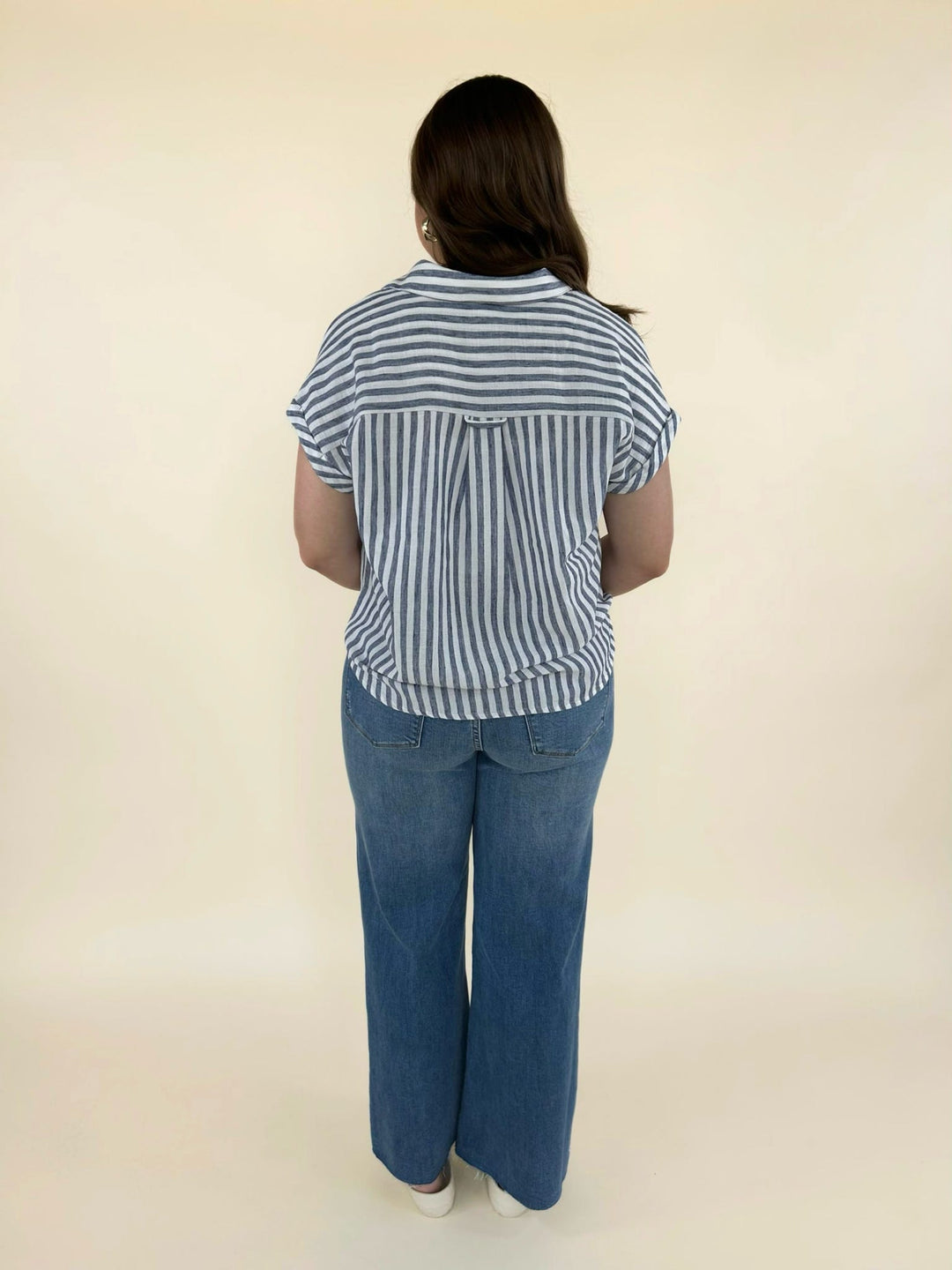 Full back view of women’s blue and white striped blouse with cap sleeves styled with wide leg denim jeans and neutral sandals