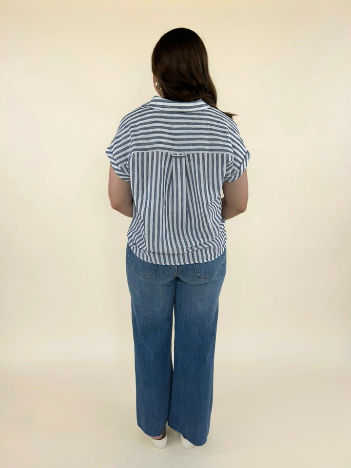 Full back view of women’s blue and white striped blouse with cap sleeves styled with wide leg denim jeans and neutral sandals
